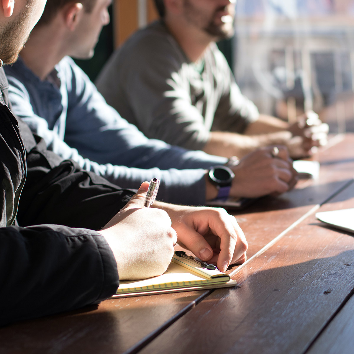 Three individuals gather at a table and take notes together.