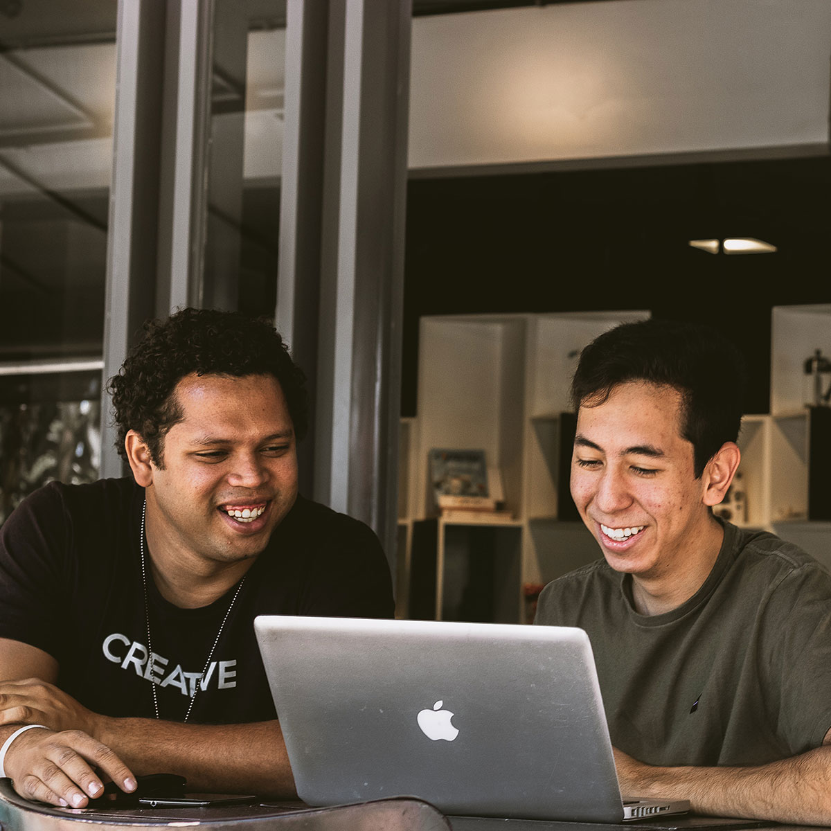 Two coworkers look at a laptop screen together and smile.