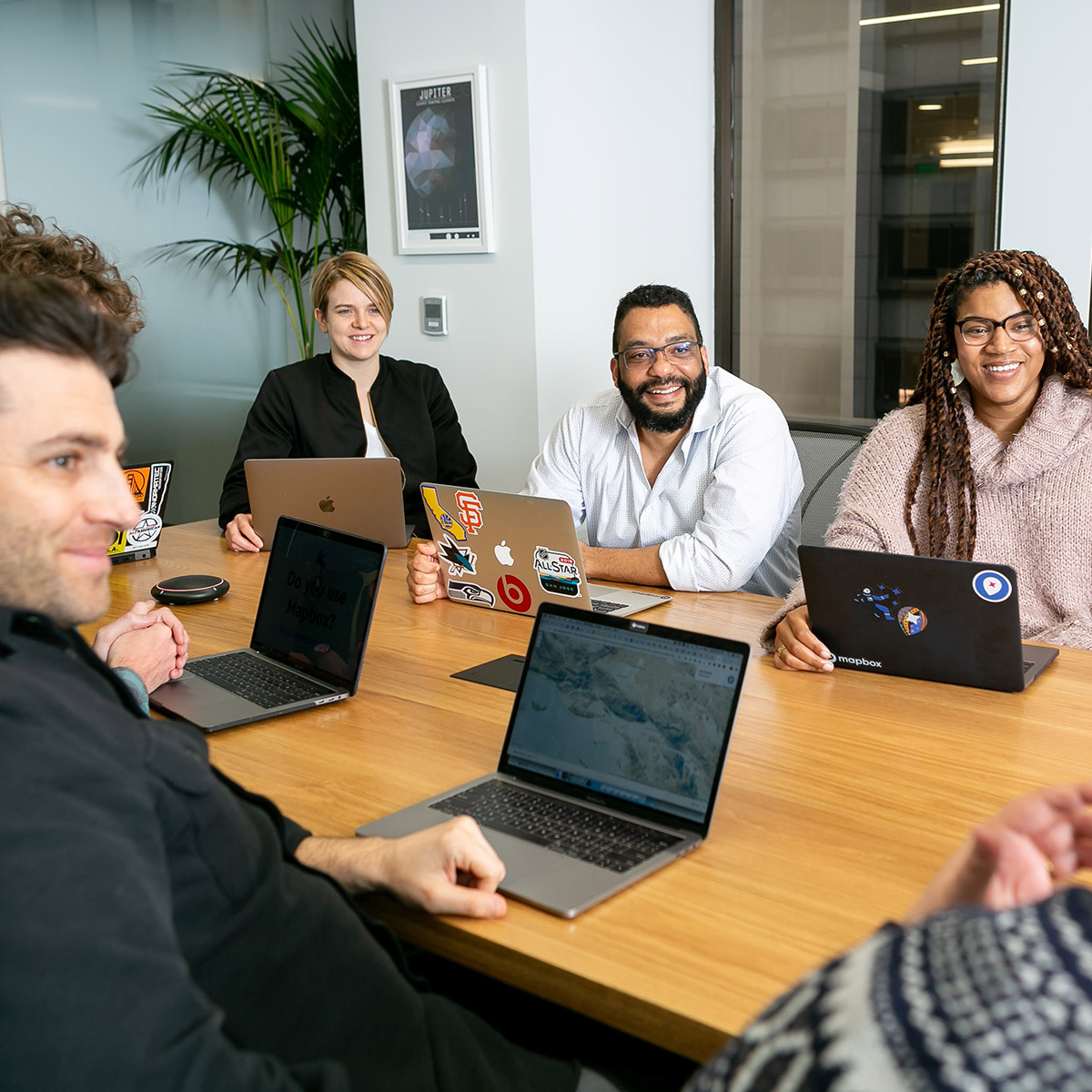 Group of diverse coworkers sit around a conference table with laptops open.