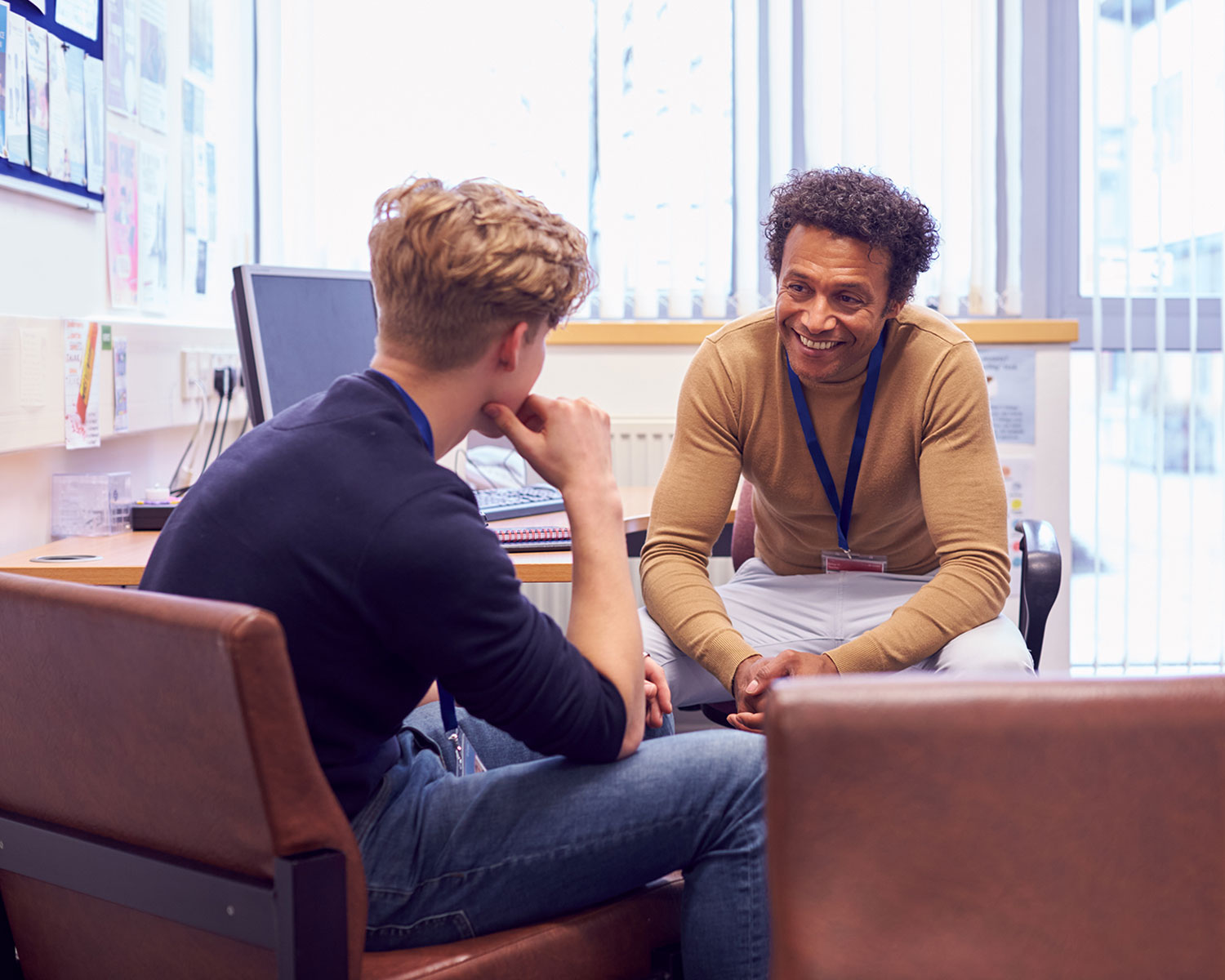 Male counselor speaks with male teenage student in his office.