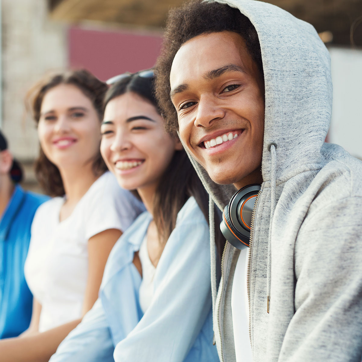 Teenage friends sit together outside and smile.