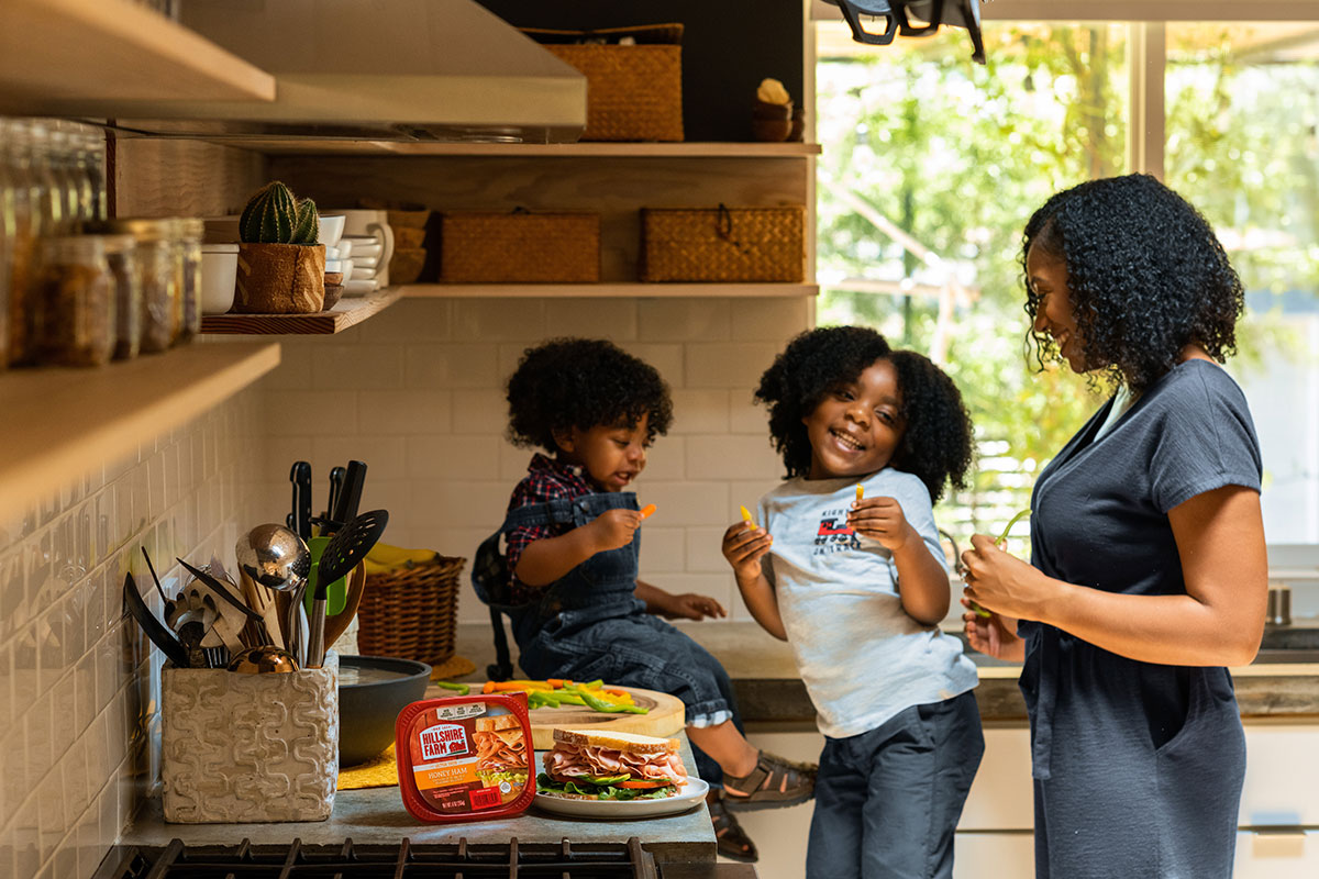 Mother and two children make sandwiches in their kitchen and laugh together.