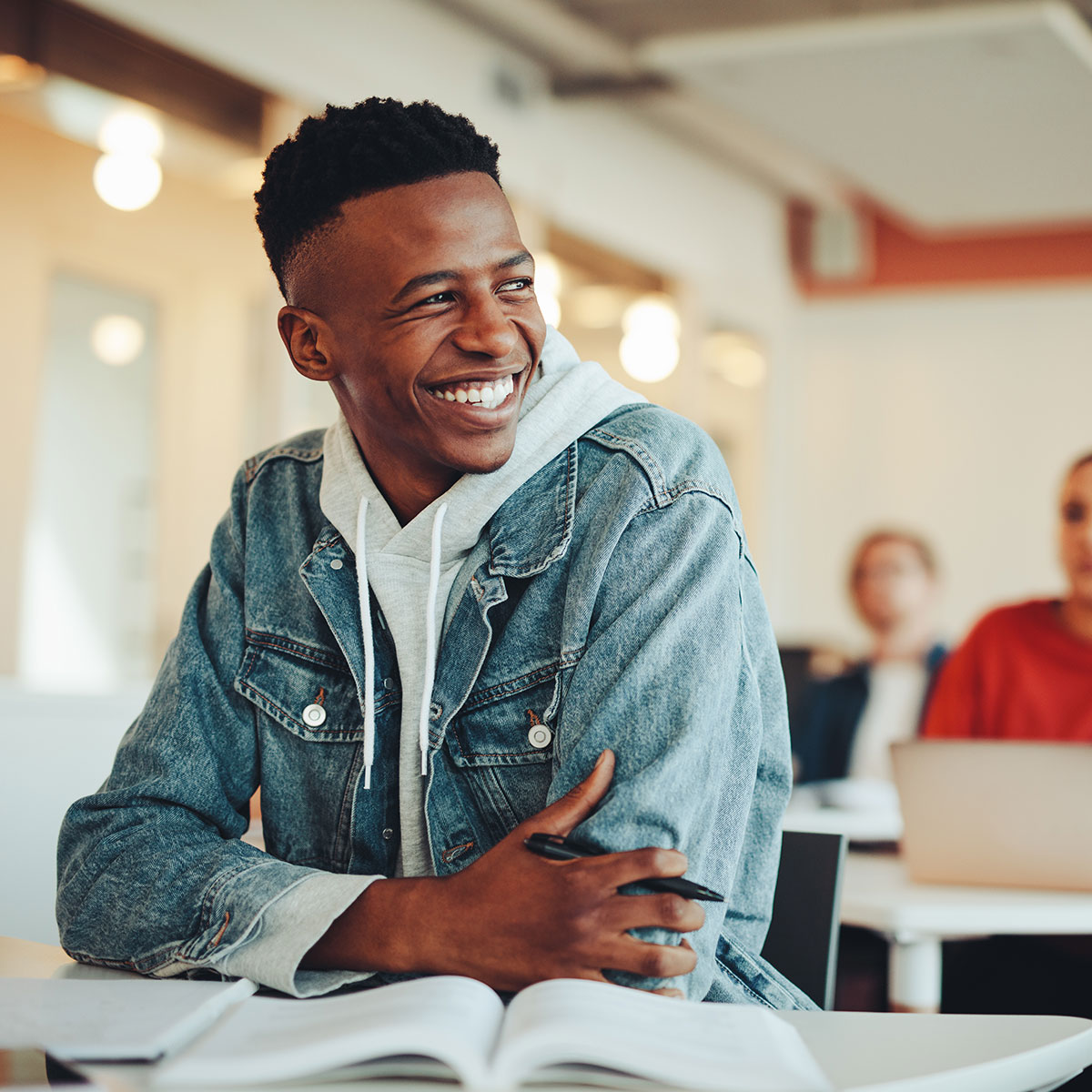 Student smiles at a desk in a classroom with his arms crossed.