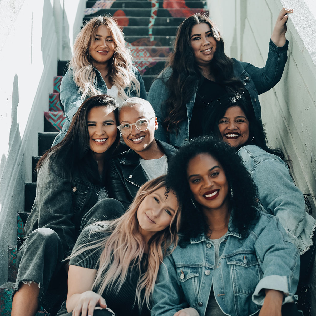 Female friends sit in a painted stairwell and smile at the camera.