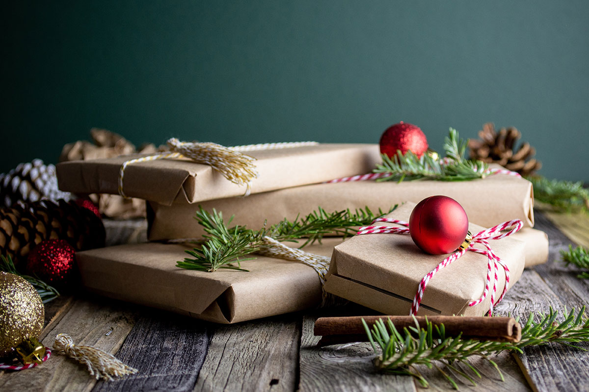 Wrapped holiday gifts sit on a table with ornaments and pinecones.