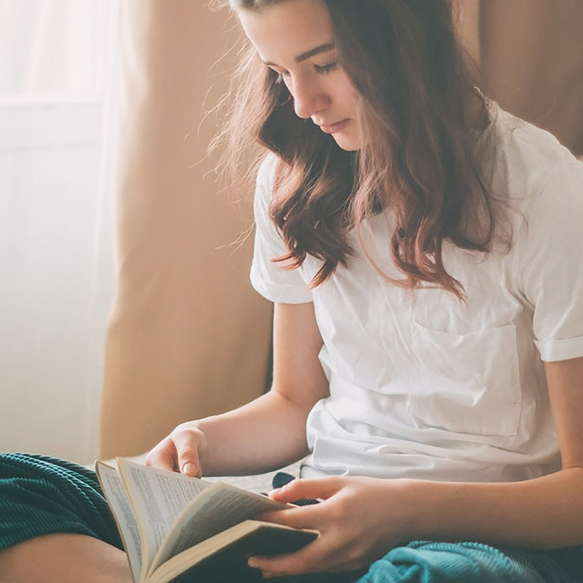 Girl sits crossed-legged reading a book.