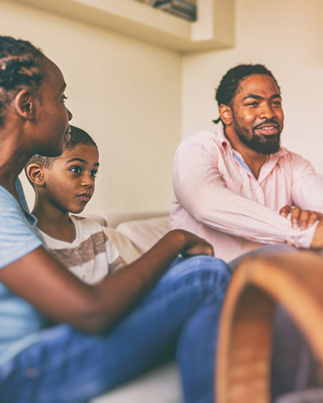 A dad and two children sit together on a couch.