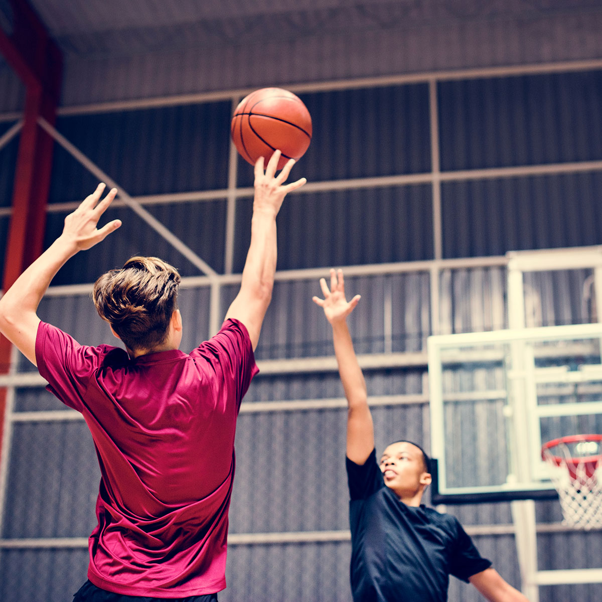 Two teenage boys play indoor basketball together.