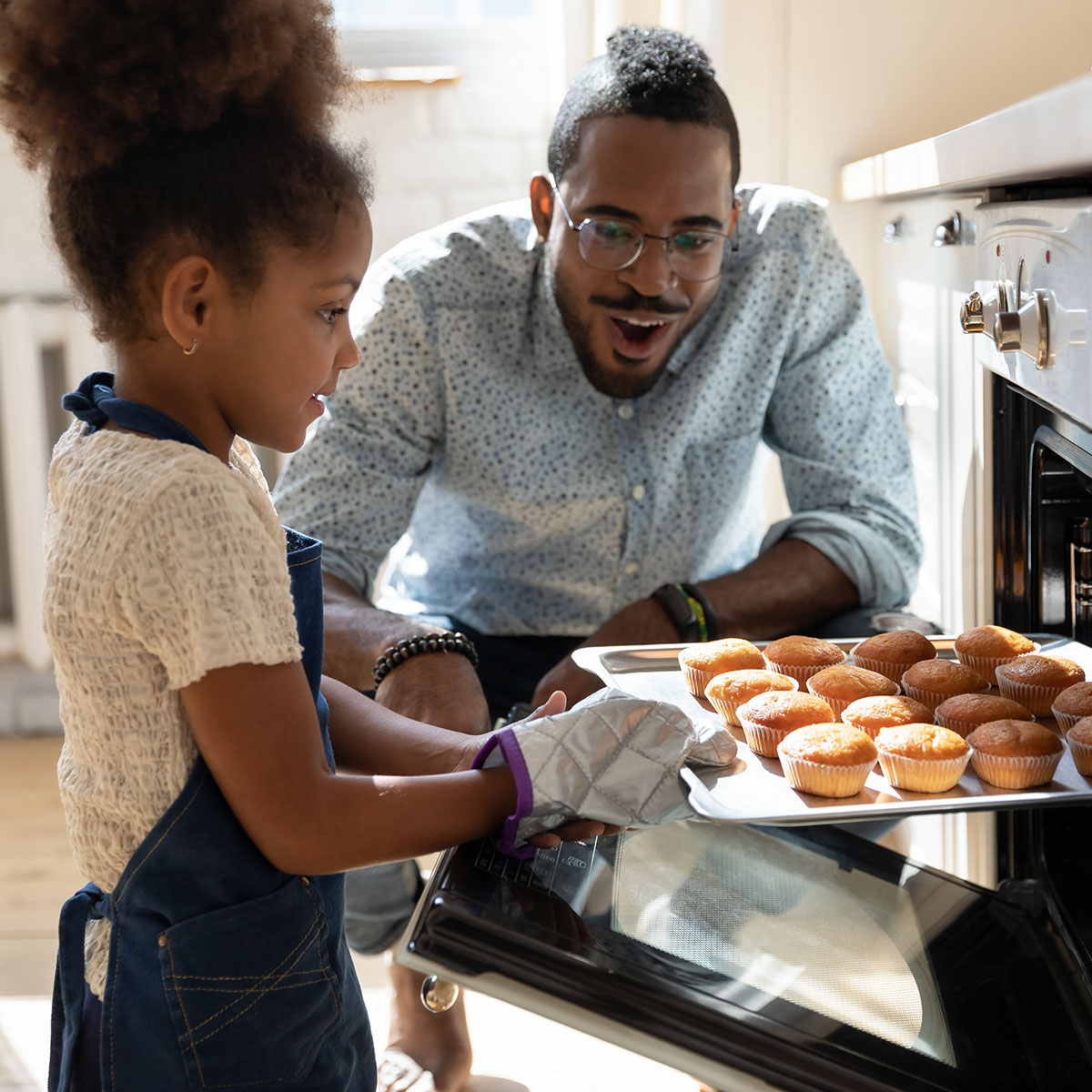 A dad and daughter bake muffins together in their kitchen.