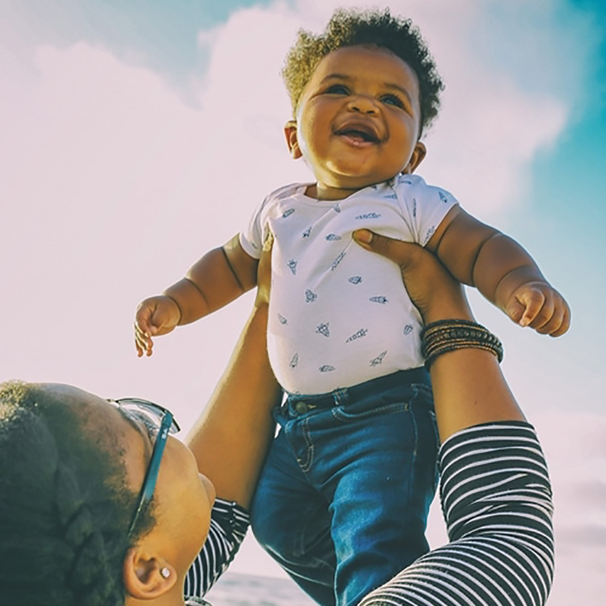 Woman lifting up her baby with sky in the background.