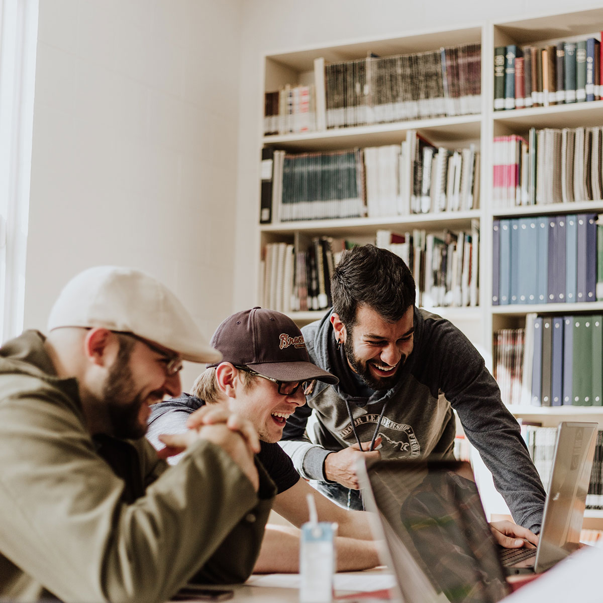 Three friends look at a computer screen and laugh together in a library.