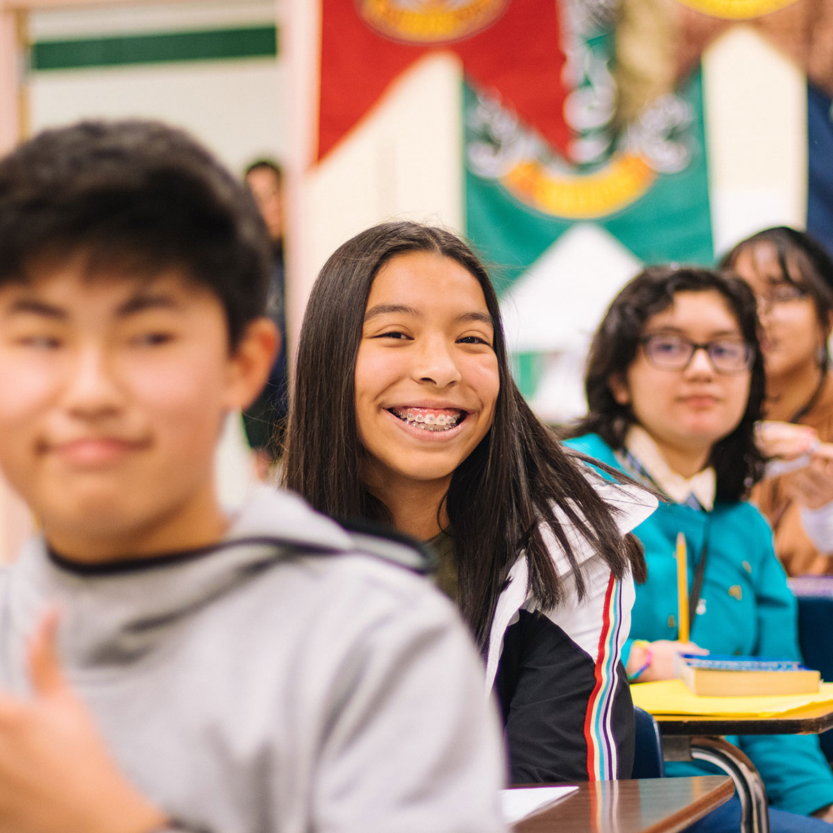 Students sit at their desks and smile in a classroom.