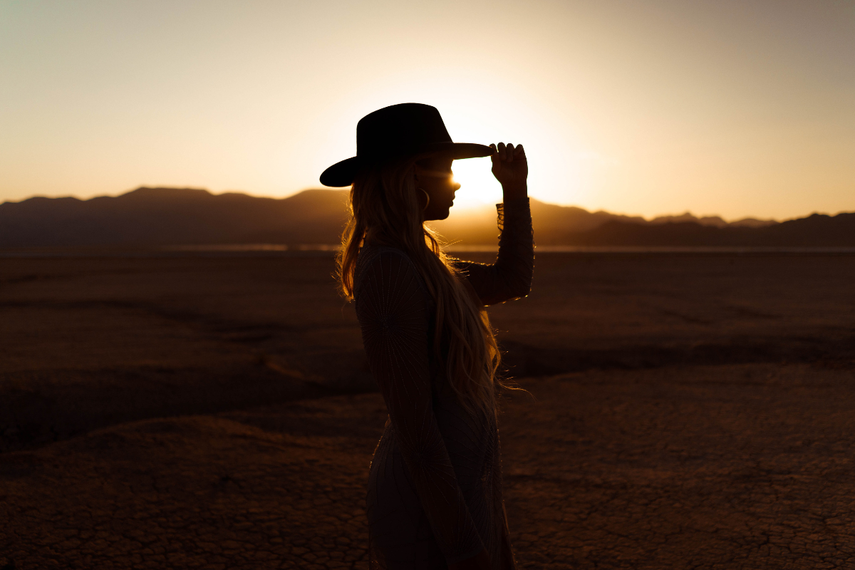 A cowboy tips her hat in the sunset.