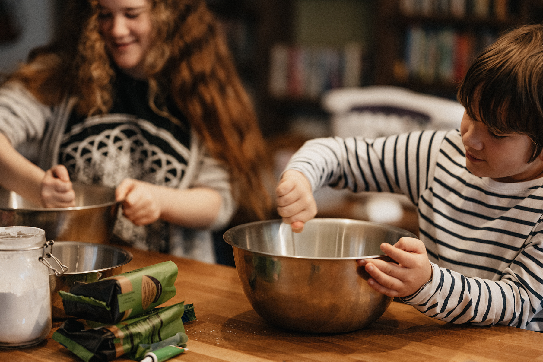 A brother and sister mix cookies in a bowl.