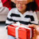 A young girl waits to open a holiday gift under a Christmas tree.